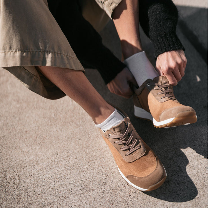 Henkilö pukee jalkaansa ruskeat tennarit ulkona.