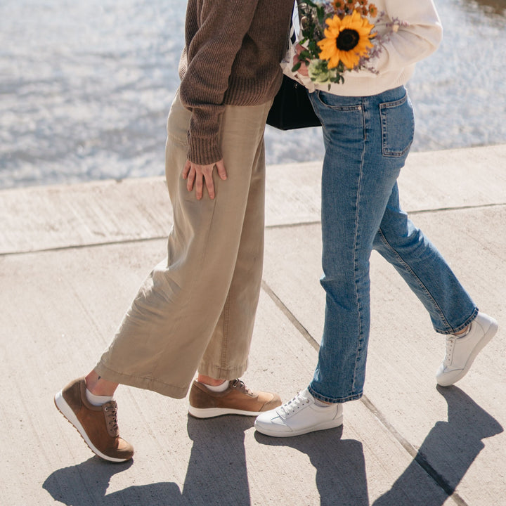 Kaksi ihmistä tervehtii toisiaan ulkona jalassaan naisten tennarit.