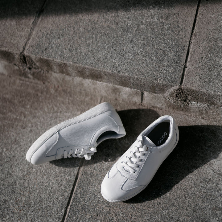 Valkoiset naisten tennarit ulkona maassa.