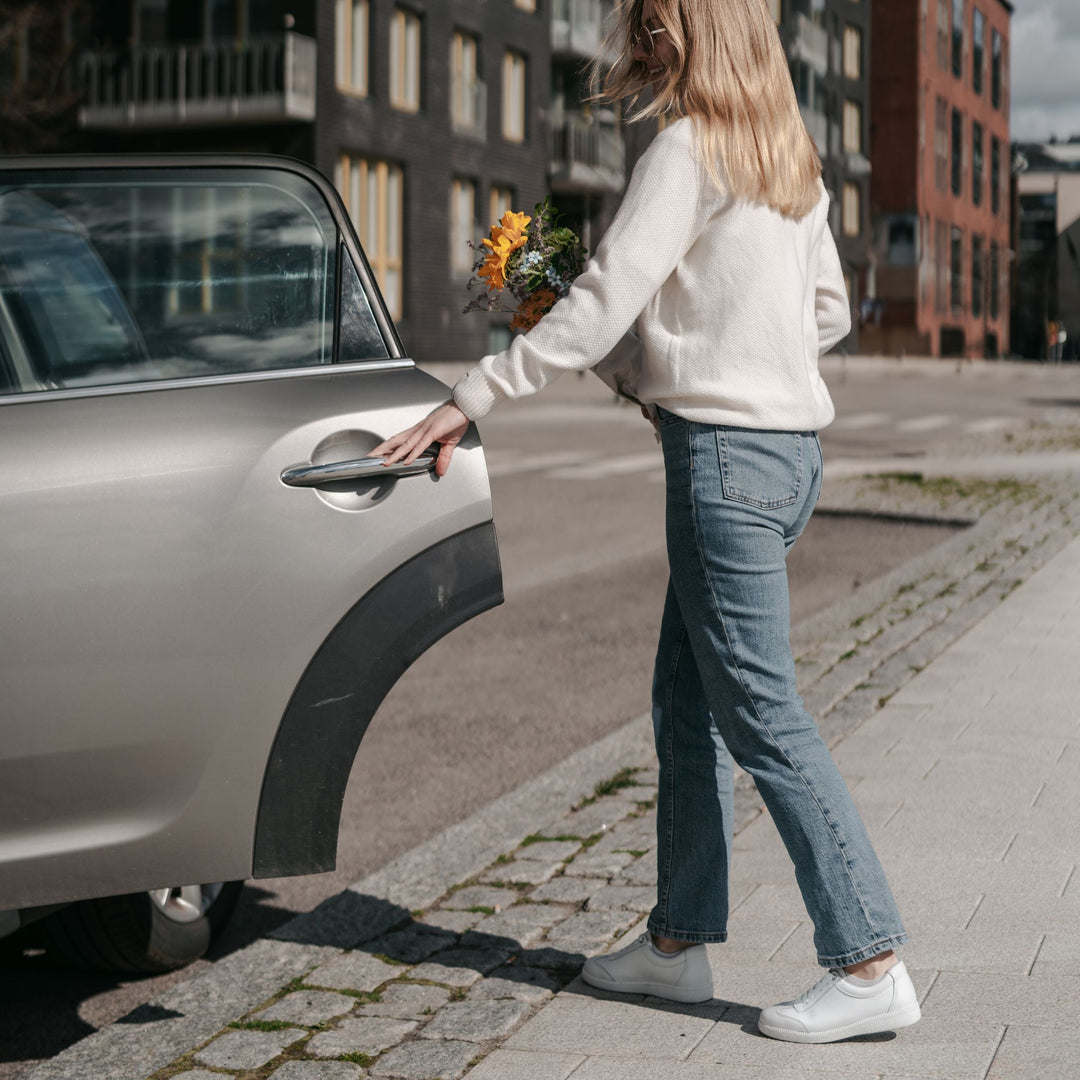 Nainen valkoisissa tennareissa avaa auton oven.