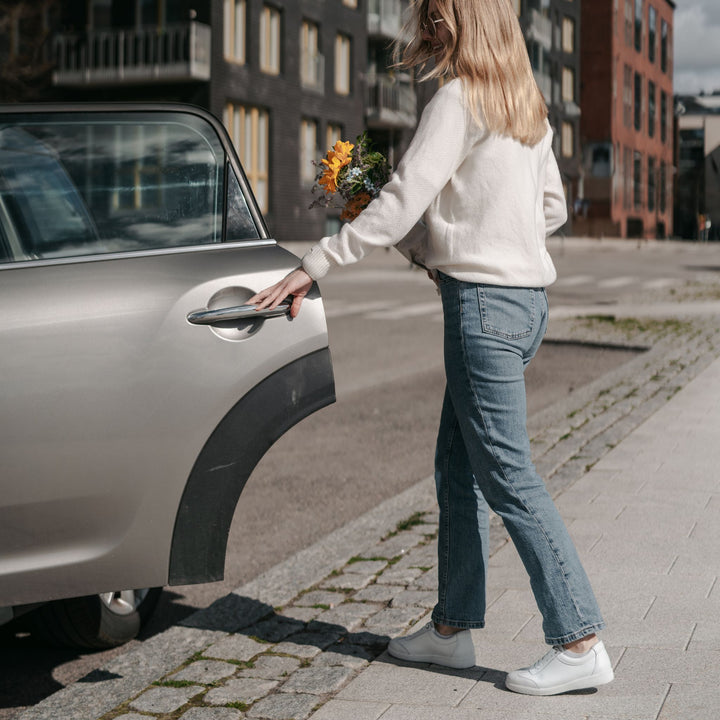 Nainen valkoisissa tennareissa avaa auton oven.
