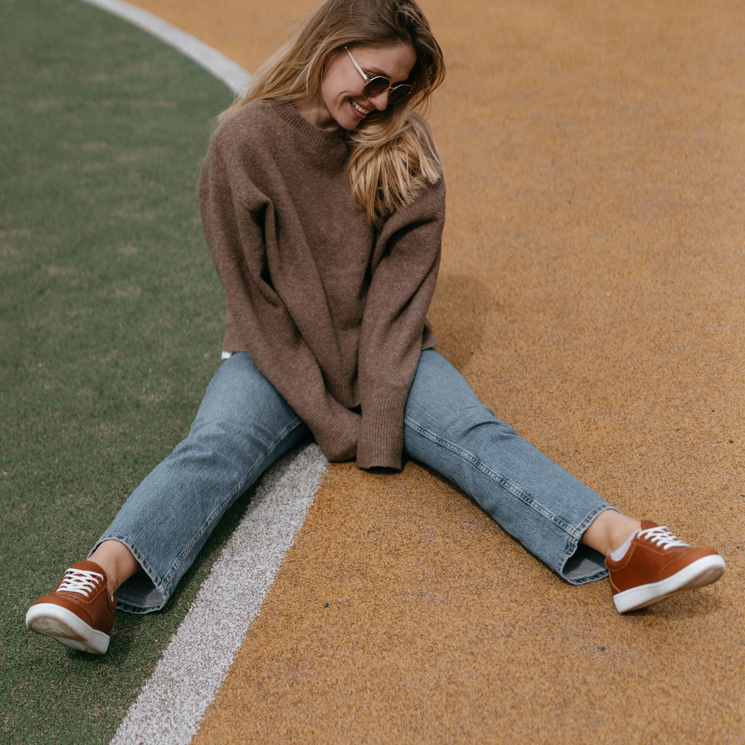 Nainen istuu iloisena maassa, jalassa nahkatennarit.