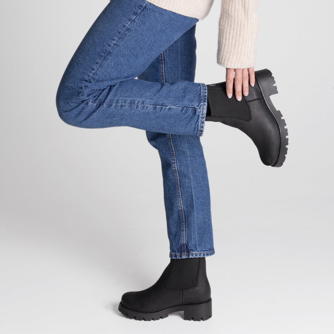 Henkilö sivusta kuvattuna, jolla jalassaan naisten mustat chelsea-nilkkurit.