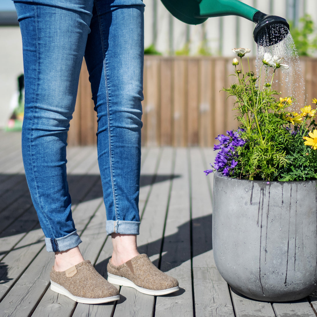 Huopatossut henkilön jalassa, joka kastelee kukkia.